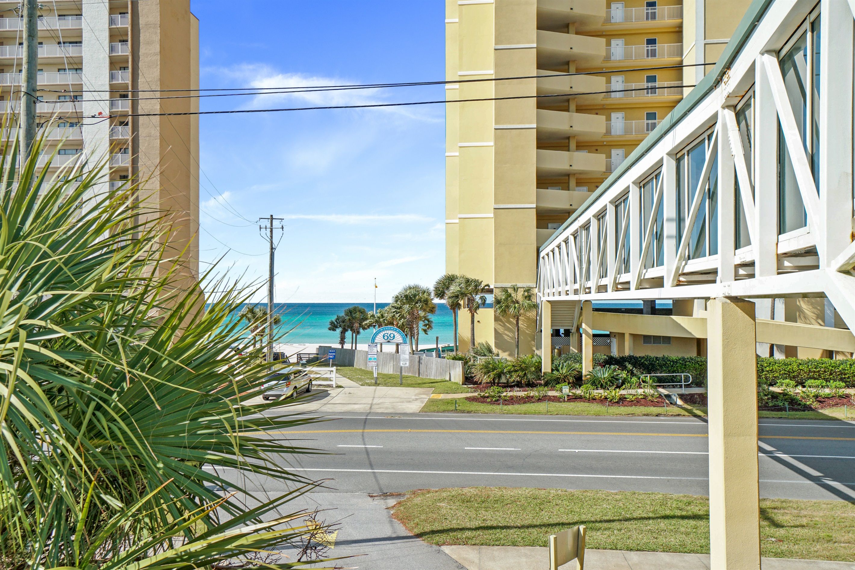 Un hotel frente al mar con vista a la playa, un puente peatonal y una zona de estacionamiento.