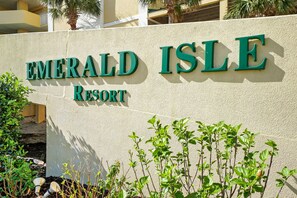 Señal de Emerald Isle Resort con una pared texturizada y follaje al frente.