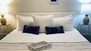 Una cama bien hecha con ropa blanca y dos almohadas, una bandeja decorativa y dos cuadros en la pared.