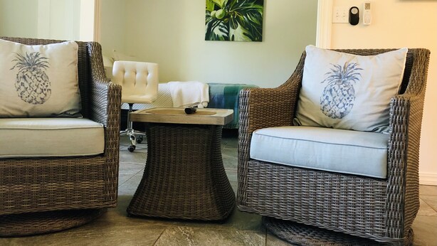 Una sala de estar con dos sillones de mimbre, una mesita y un sillón blanco.