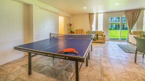 Una mesa de ping pong con red en una habitación con vistas a un césped verde y un edificio al fondo.
