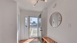 A hallway with a wooden bench, a round mirror, and a view through a glass door to an outdoor area. - Carter Street | Walkable Crozet | Pet-Friendly (Crozet)