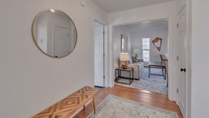 A hallway with a round mirror, a bench, and a rug leading to a living area with a sofa, a table, and a lamp. - Carter Street | Walkable Crozet | Pet-Friendly (Crozet)
