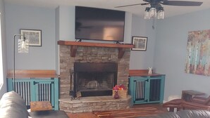 Un salon doté d’une cheminée en pierre, d’un ventilateur de plafond et d’un grand téléviseur à écran plat fixé au-dessus de la cheminée.