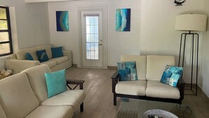 A living room with two sofas, a coffee table, and a floor lamp. There is a door with a window, and two abstract paintings on the wall. - Entire Villa for Rent, Leeward / Grace Bay, Short Walk to Sunset Beach (Providenciales)