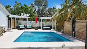 A rectangular swimming pool with a white deck, surrounded by a white picket fence and various plants.