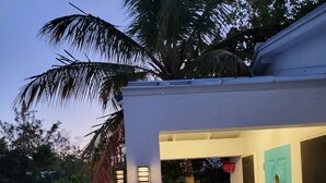 A small, white building with a turquoise door, a tiled patio, and a palm tree in the background. - Entire Villa for Rent, Leeward / Grace Bay, Short Walk to Sunset Beach (Providenciales)