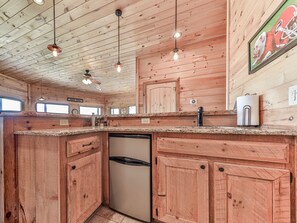 Ein Holzhütten-Interieur mit Küchenbereich, der einen eingebauten Geschirrspüler, Holzschränke und Pendelleuchten zeigt.