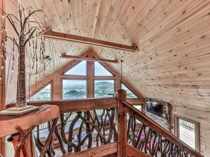 A wooden interior with a high ceiling, a wooden railing, and a view of the landscape through large windows.