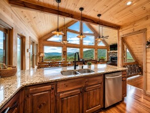Una cocina amplia con encimeras de granito, armarios de madera y ventanas grandes que ofrecen vistas a las montañas.