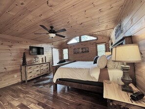 Ein Schlafzimmer in einer Holzhütte mit Bett, Kommode, Fernseher und Deckenventilator.