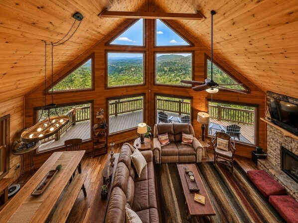 A spacious loft-style room with a large wooden ceiling, a cozy seating area with a sofa and armchairs, a dining table, and a fireplace. - Blue Ridge Mountaintop Cabin with a Stunning View, Hot Tub, Pool Table, Fire Pit (Blue Ridge)
