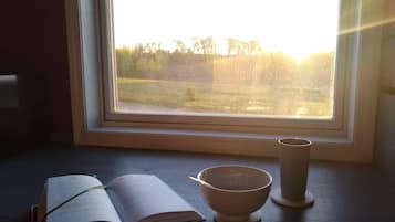 Une pièce avec une fenêtre donnant sur un champ verdoyant, un livre et un bol en céramique posé sur une table en bois.
