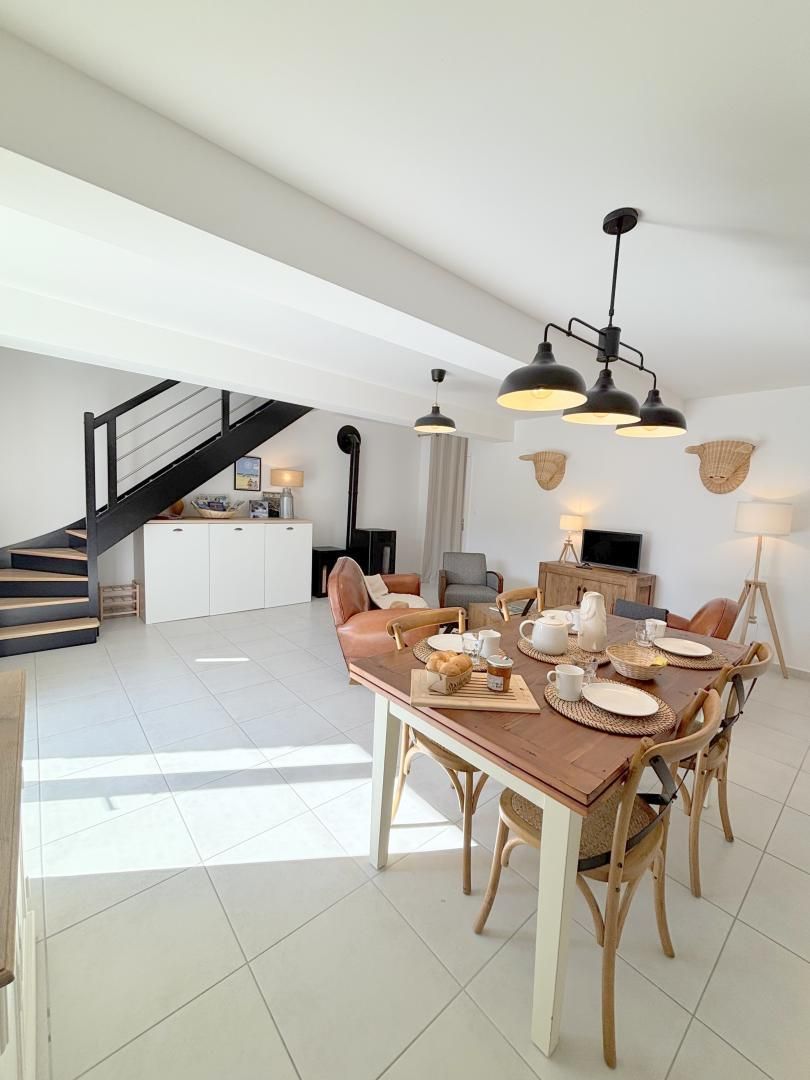 A modern dining area with a wooden table set for four, surrounded by wicker chairs. A staircase with black railings leads to an upper level.