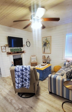 Un salon doté d’un ventilateur de plafond, d’un téléviseur, d’une cheminée et d’une décoration sur le thème de la plage.