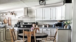 Keittiössä on valkoiset kaapit, liesi, mikroaaltouuni sekä ruokailutila, jossa on puutuoleja ja pöytä.