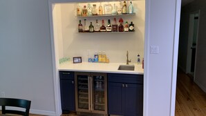 A compact kitchen with a bar area featuring shelves of liquor bottles, a refrigerator, and a sink.