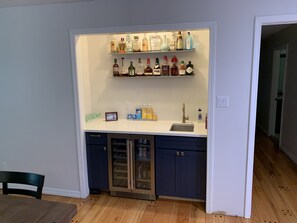 A compact kitchen with a bar area featuring shelves of liquor bottles, a refrigerator, and a sink.