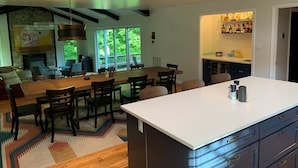 A modern kitchen with a large island, dining area, and a stone fireplace.