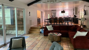A spacious living room with a large sectional sofa, a coffee table, and a dining area with a kitchen in the background.