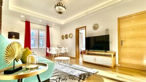 A modern living room with a sofa, coffee table, and TV. There is a dining area with chairs and a table, and a wooden cabinet with a TV. - Huertas II - 2 bedrooms, in the best area (Madrid)