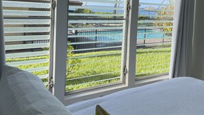 Ein Schlafzimmer mit einem großen Bett, Blick auf einen Pool und einem Balkon mit Geländer.