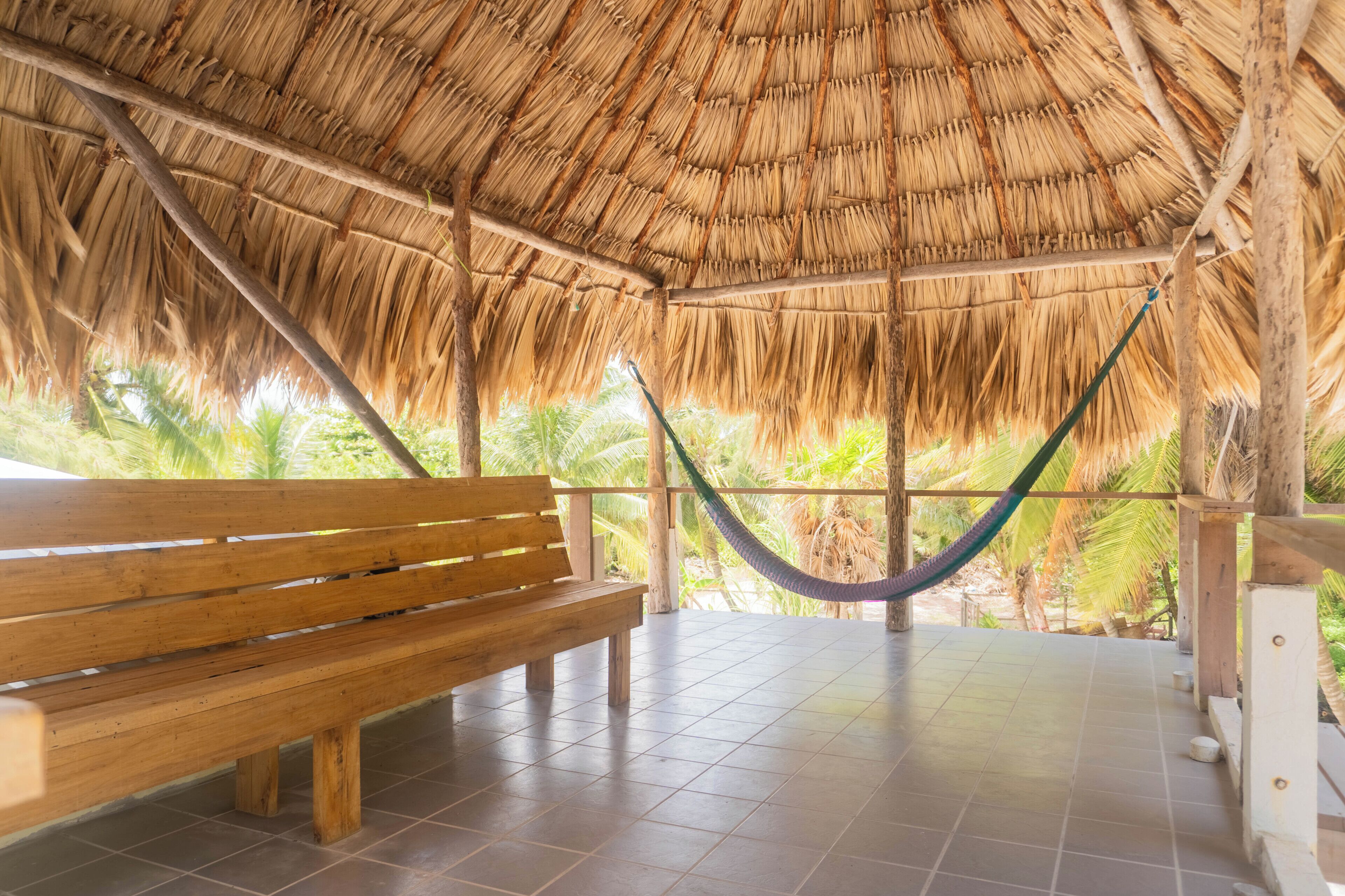 A wooden bench and a hammock under a thatched roof structure.