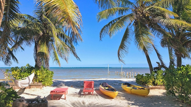 Una playa con una hamaca, una silla roja y dos kayaks amarillos.