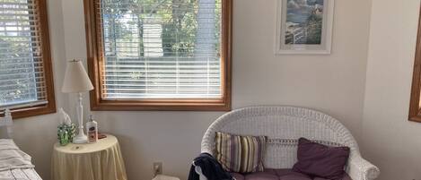 A bedroom with a wicker sofa, a bedside table with a lamp, and a framed picture on the wall.