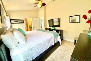 A bedroom with a bed, a television, a desk, and a ceiling fan.