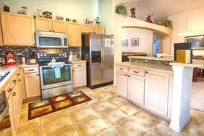 Una cocina con armarios de madera, electrodomésticos de acero inoxidable y piso de baldosas.