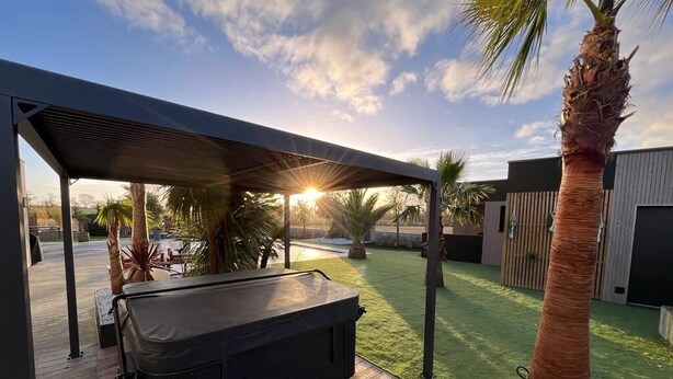 Ein Whirlpool unter einer Pergola mit Blick auf einen Garten und ein Gebäude im Hintergrund.