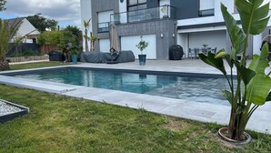 Ein modernes, zweistöckiges Haus mit Swimmingpool, Sitzgelegenheiten im Freien und einer überdachten Grillanlage.