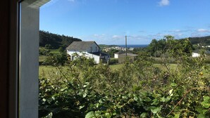 A view through a window of a white building with a sloped roof, surrounded by greenery and a clear blue sky. - Country house with gate next to the sea (Santa Marta de Ortigueira)