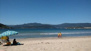 A beach with a clear sky, a person standing by the water, and a beach umbrella. - Country house with gate next to the sea (Santa Marta de Ortigueira)