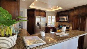 A kitchen with dark wooden cabinets, a granite countertop, a refrigerator, a microwave, and a potted plant. - PGA WEST PALMER GATE - 9TH HOLE - JUST FORE FUN  (La Quinta)