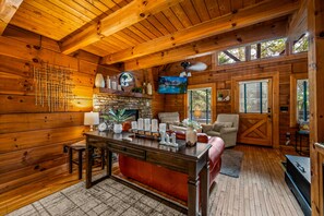 A cozy cabin interior with a wooden interior, a stone fireplace, a dining area, and a TV mounted on the wall.