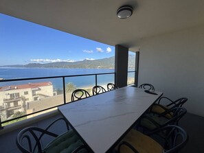 A balcony with a table and chairs, overlooking a body of water and distant land.