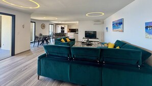 Een moderne woonkamer met een groene zithoek, een eethoek en een keuken op de achtergrond.
