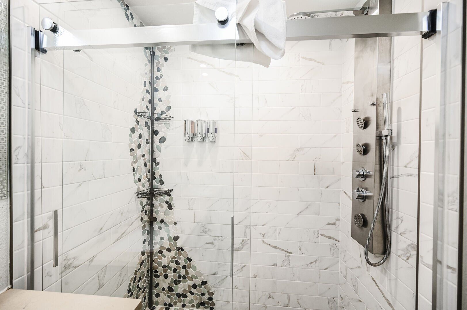 A modern shower with a glass door, a towel rack, and a handheld showerhead.