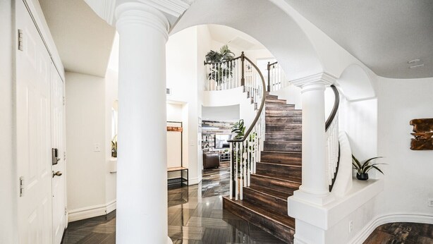 A spacious hallway with a wooden staircase, white columns, and a modern interior design. - SVS: Spacious 6BD Vegas Home | Private Pool, BBQ & Game Room | Sleeps 12 (Henderson)