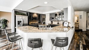 A modern kitchen with a central island, dark cabinetry, stainless steel appliances, and a bar area with stools. - SVS: Spacious 6BD Vegas Home | Private Pool, BBQ & Game Room | Sleeps 12 (Henderson)