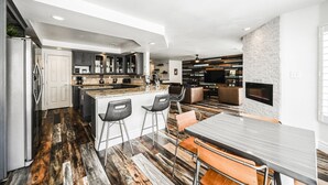 A modern kitchen with dark cabinets, a large island, and a bar area with stools. - SVS: Spacious 6BD Vegas Home | Private Pool, BBQ & Game Room | Sleeps 12 (Henderson)