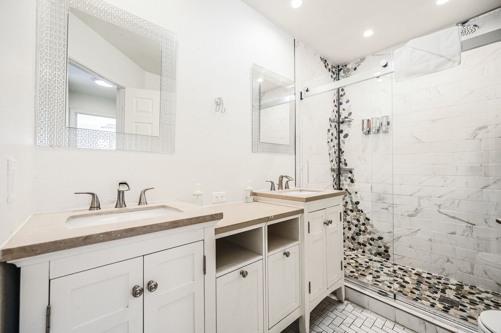 A modern bathroom with two sinks, a shower, and a glass-enclosed shower area.
