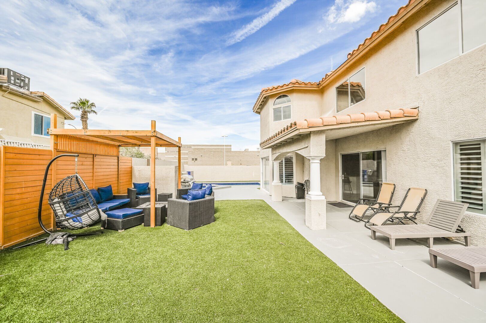 A backyard with artificial grass, a wooden pergola, outdoor furniture, and a pool.