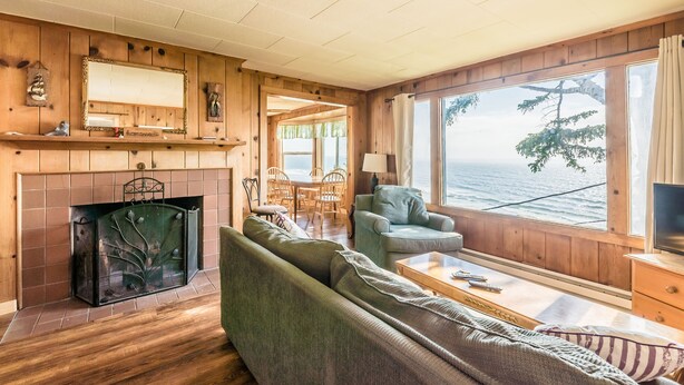 Un salón acogedor con chimenea, paredes de madera, un sofá, una mesita de centro y vistas al mar.