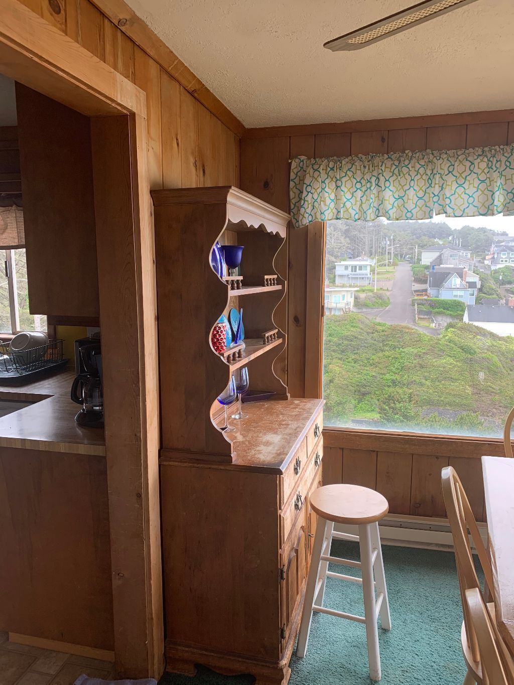 Une cuisine avec des meubles en bois, une machine à café et une vue sur un quartier résidentiel, visible par une fenêtre.