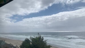 Una playa con olas, cielo nublado y casas al frente.