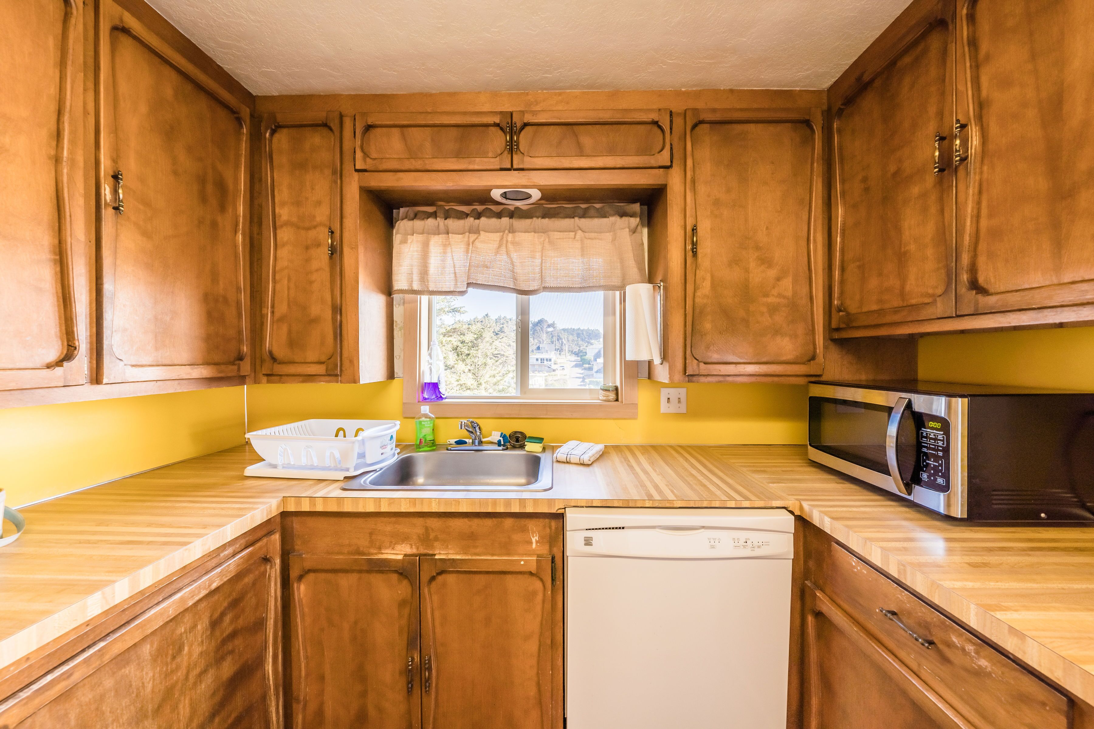 Une cuisine compacte avec des meubles en bois, un lave-vaisselle blanc, un four à micro-ondes et une fenêtre donnant sur l’extérieur.