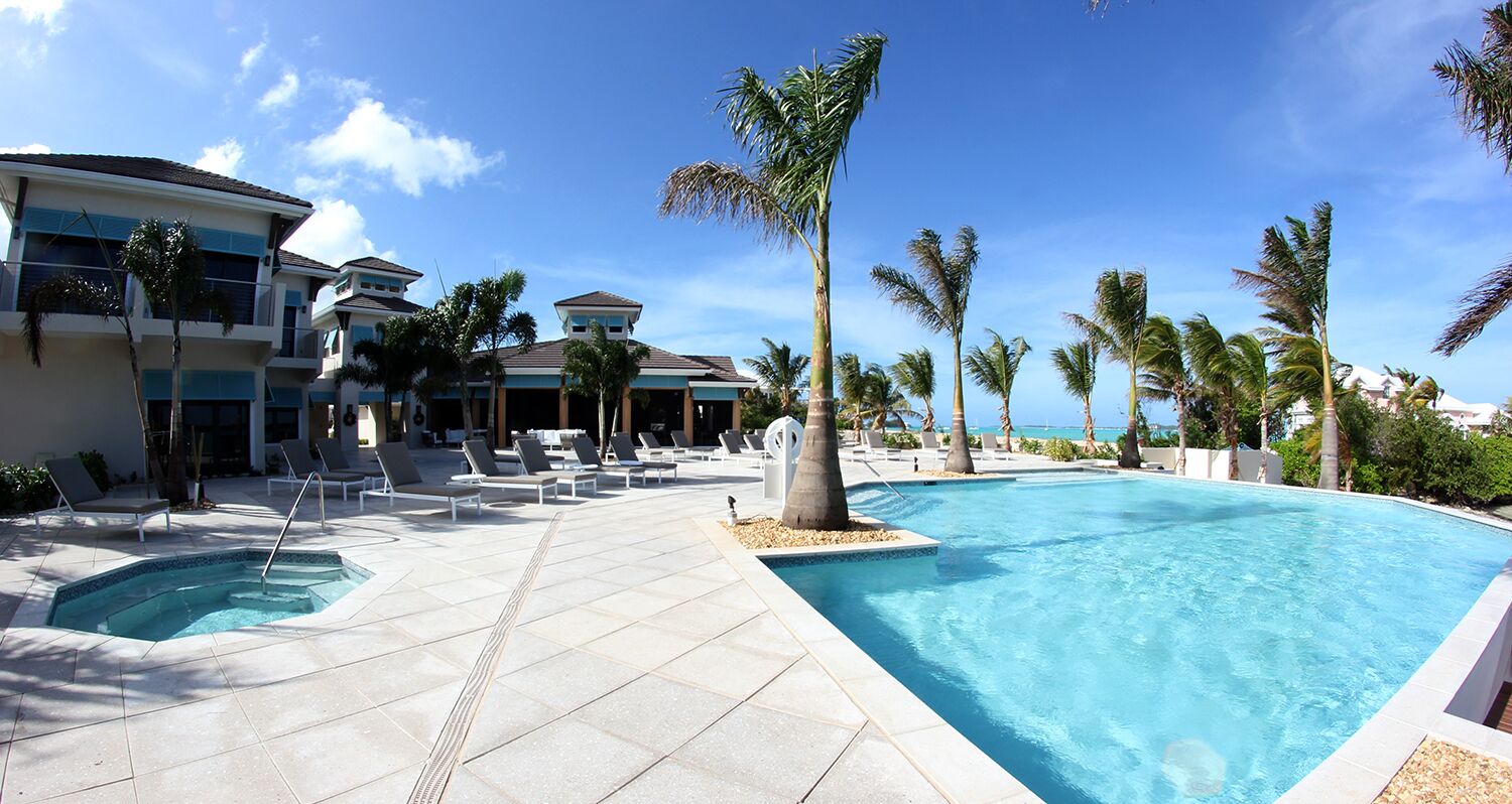 Zona de piscina de un complejo turístico con varias piscinas, sillones de descanso y palmeras.